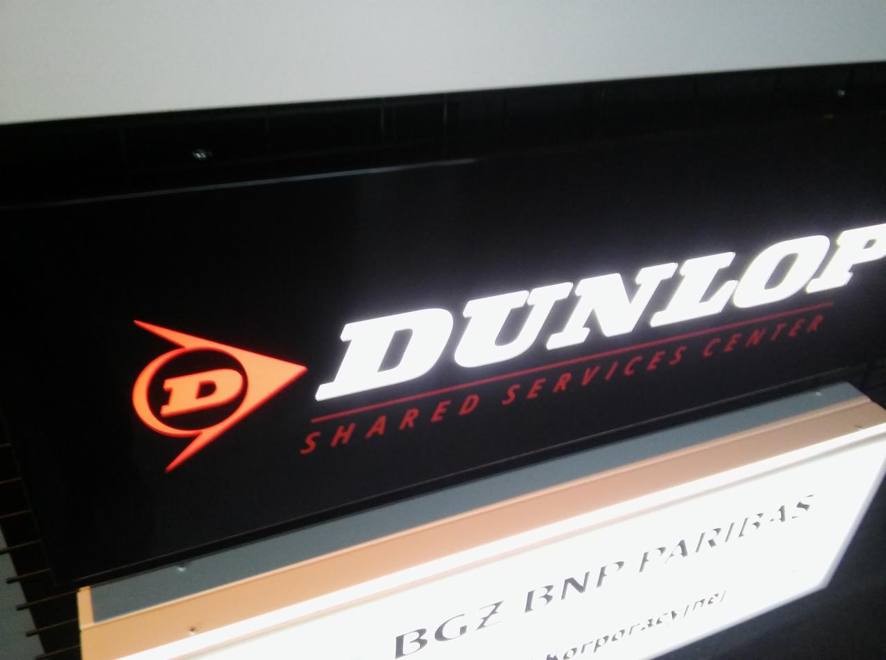 Podświetlane logo Dunlop Shared Services Center na czarnym tle, widoczne logo BNP Paribas poniżej.