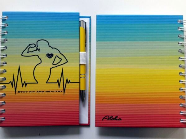 Dwa notatniki spiralne z kolorowym gradientem, jeden z nadrukiem sylwetki osoby ćwiczącej, linią życia i napisem 'Stay fit and healthy', drugi z napisem 'Aloha'. Do pierwszego dołączony długopis.