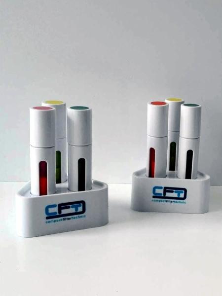 Dwa białe stojaki z logo CFT, każdy z trzema białymi cylindrami z kolorowymi wierzchołkami (czerwony, żółty, zielony) i czarnymi paskami na boku, na białym tle.