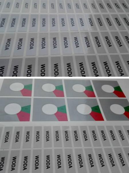 Arkusze z powtarzalnymi etykietami z napisami 'WODA' i 'AZOT' oraz kwadratowe naklejki z białym okręgiem i kolorowymi fragmentami w rogach, ułożone pod kątem.