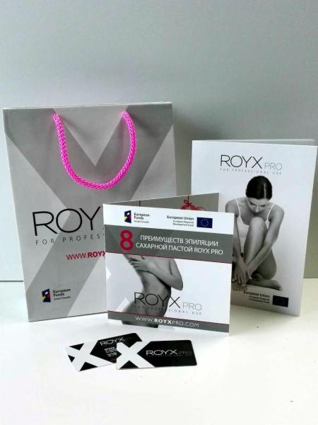 Zestaw materiałów reklamowych ROYX PRO: torba z różowymi uchwytami, ulotka z informacją o 8 zaletach depilacji pastą cukrową, broszura z wizerunkiem kobiety oraz dwie wizytówki z logo firmy.