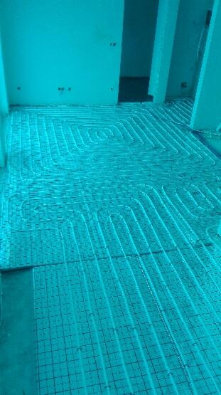 Rozłożona instalacja ogrzewania podłogowego na siatce montażowej w surowym wnętrzu, widoczne pętle rur przed zalaniem wylewką.