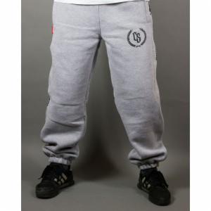 Szare spodnie dresowe z czarnym logo CS na udzie, noszone przez osobę w czarnych sportowych butach na szarym tle.
