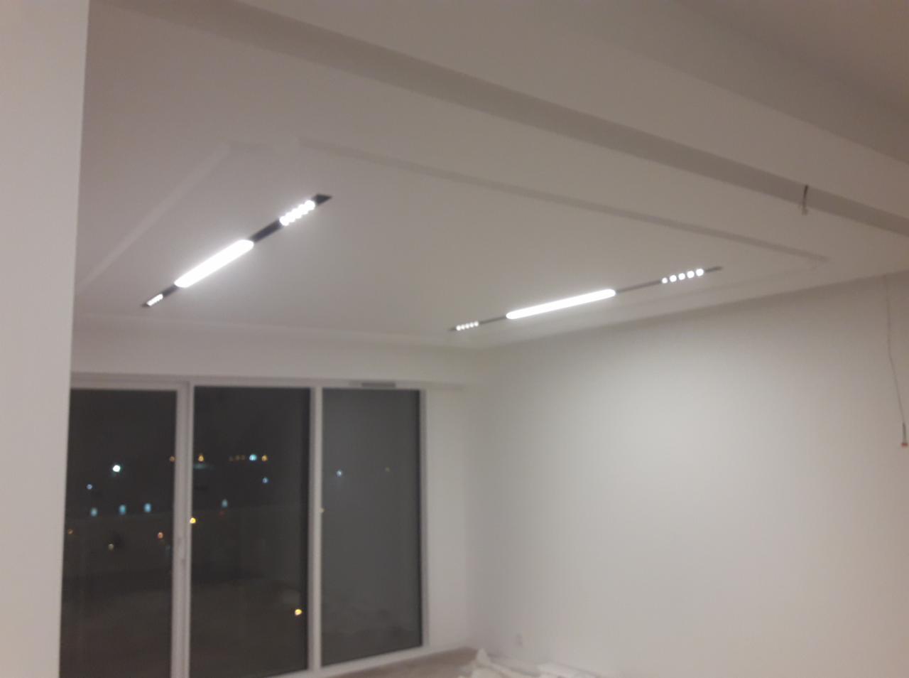 Nowoczesne oświetlenie LED wkomponowane w sufit podwieszany w jasnym, minimalistycznym wnętrzu z dużymi oknami balkonowymi.