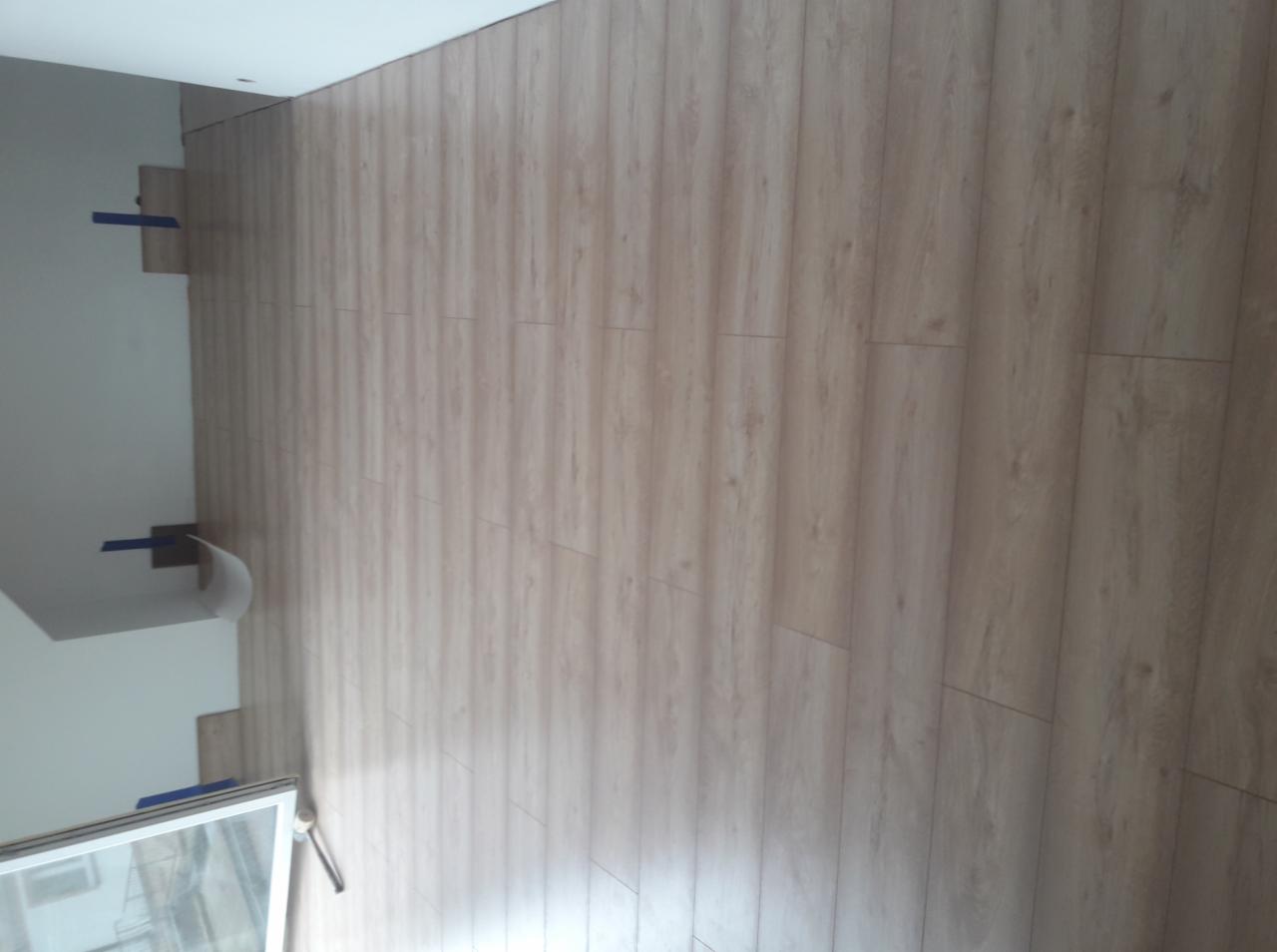 Ściana wewnętrzna wykończona panelami imitującymi drewno, widoczne fragmenty okna i ściany w trakcie prac wykończeniowych z użyciem taśmy malarskiej.