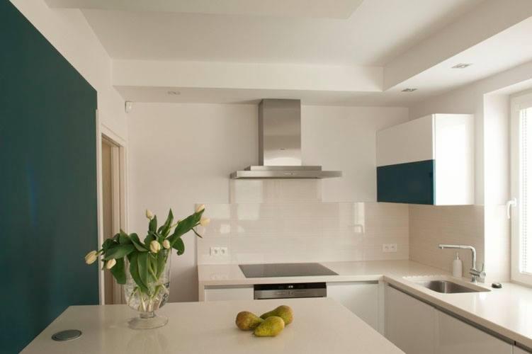 Nowoczesna kuchnia z białymi szafkami, blatem z konglomeratu i akcentem w postaci turkusowej ściany oraz szafki. Na blacie wazon z białymi tulipanami i trzy zielone gruszki.