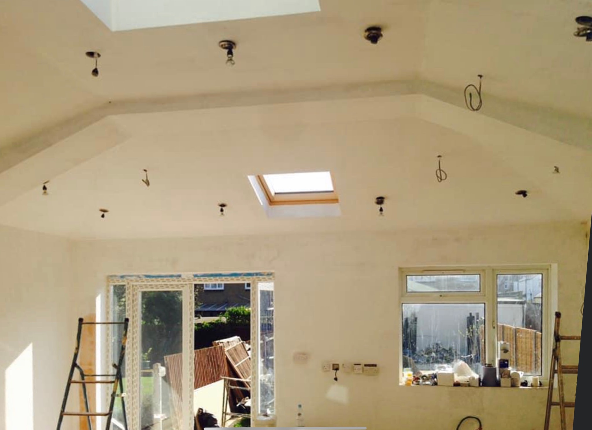 Wnętrze w trakcie remontu z widocznymi punktami oświetleniowymi w suficie, oknem dachowym i rozłożoną drabiną opartą o ścianę.