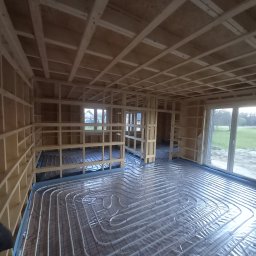 COP Łódź Beata Latkowska - Wnętrze domu w trakcie budowy z widoczną drewnianą konstrukcją szkieletową i rozłożonym systemem ogrzewania podłogowego na folii izolacyjnej.