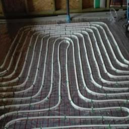 COP Łódź Beata Latkowska - Białe rury ułożone w pętle na metalowej siatce, instalacja ogrzewania podłogowego w trakcie montażu, widoczne materiały izolacyjne i elementy konstrukcyjne budynku.