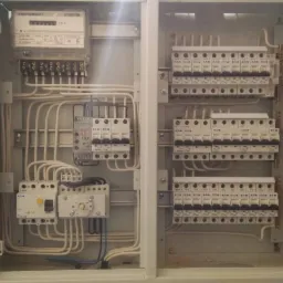 Otwarta skrzynka elektryczna z licznikiem, bezpiecznikami i przewodami wewnątrz, widoczne elementy marki Eaton.