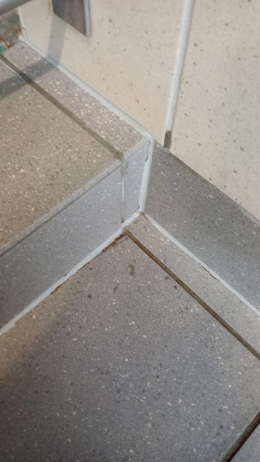 Szczegółowe ujęcie narożnika z szarych płytek podłogowych i listwy przypodłogowej, z widocznymi śladami brudu przed czyszczeniem fug.