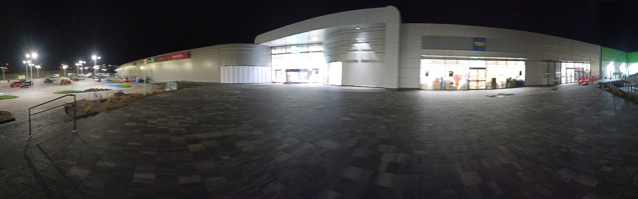 Panorama nowoczesnego budynku handlowego oświetlonego nocą, widok z brukowanego placu.