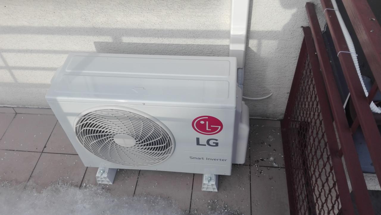 Zewnętrzna jednostka klimatyzacji LG Smart Inverter zamontowana na wspornikach przy ścianie budynku, widoczne elementy instalacji.