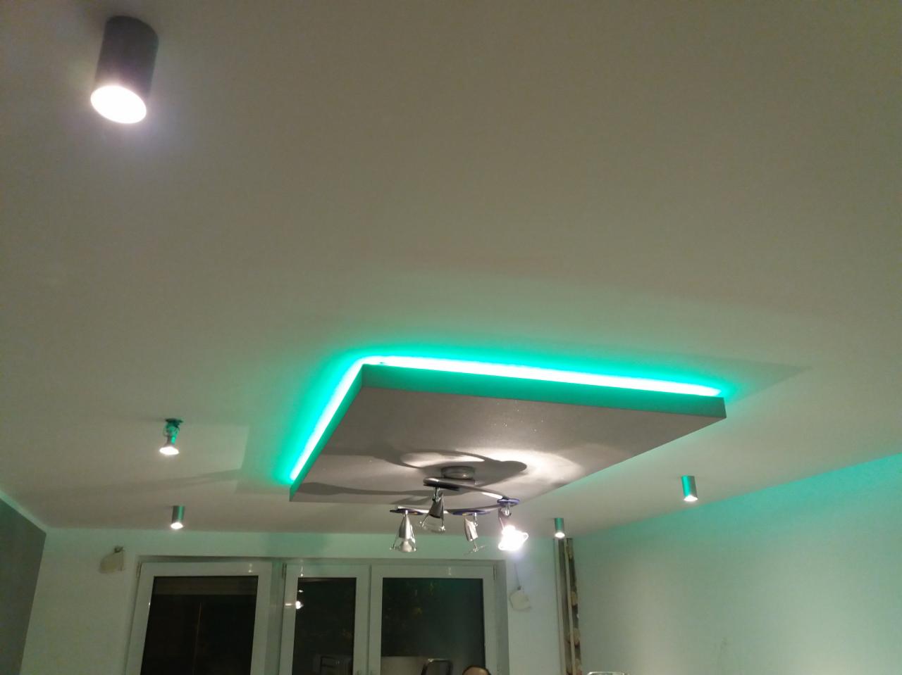 Podwieszany sufit z oświetleniem LED w kolorze zielonym, centralny punkt z reflektorami, dodatkowe punkty świetlne w suficie.