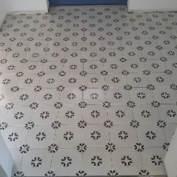 Świeżo ułożona podłoga z płytek w biało-czarny wzór, widok na próg drzwiowy z niedokończonymi ościeżnicami.