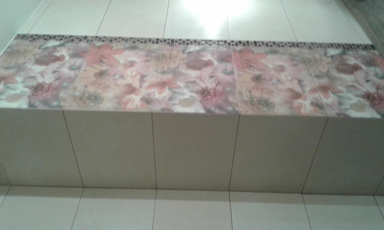 Półka w łazience wyłożona płytkami z motywem kwiatowym, obramowana mozaiką z drobnych płytek, widok z dołu.