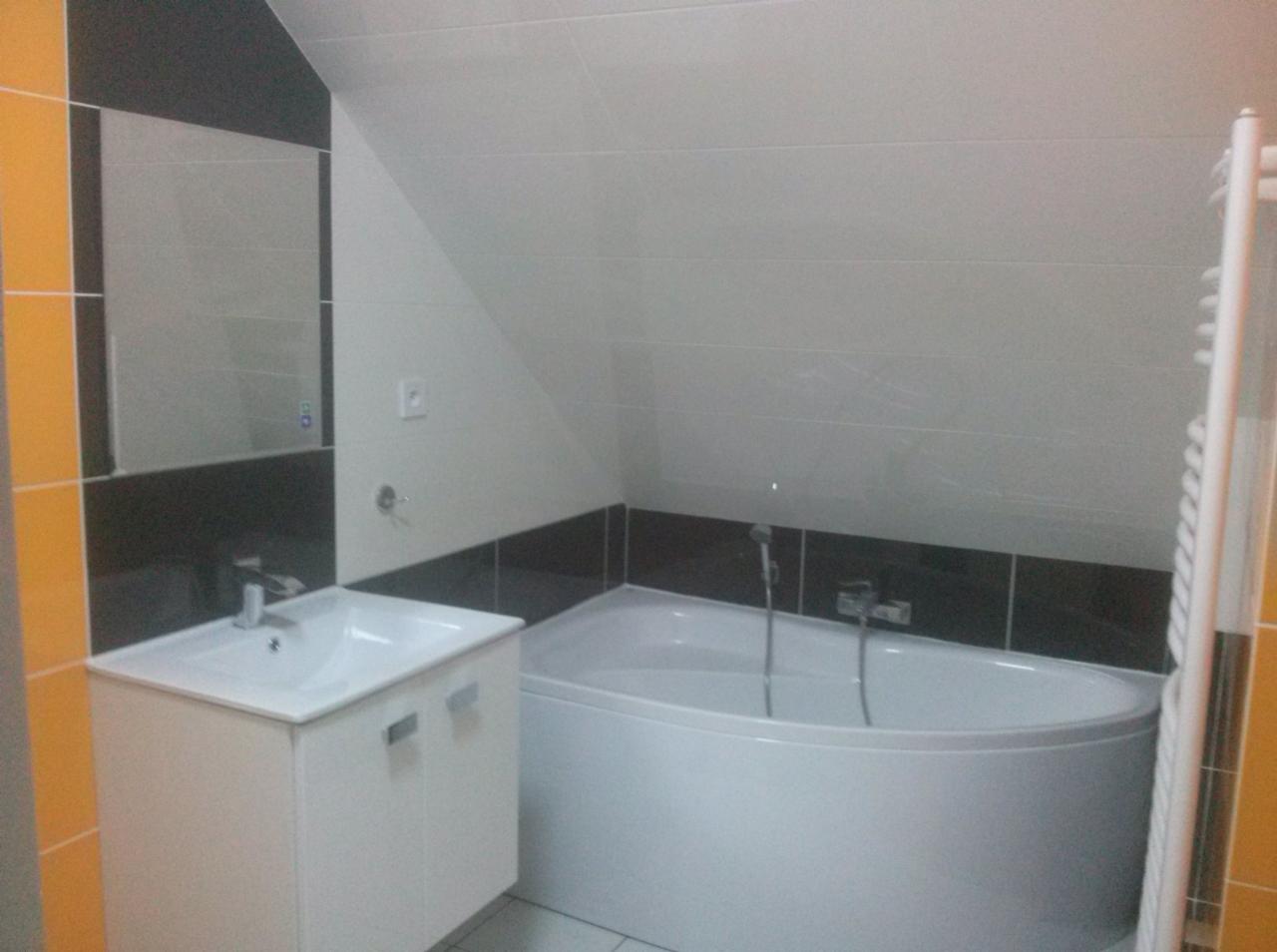 Nowoczesna łazienka na poddaszu z wanną narożną, umywalką z szafką i lustrem, wykończona białymi i czarnymi płytkami, z widocznym grzejnikiem drabinkowym.