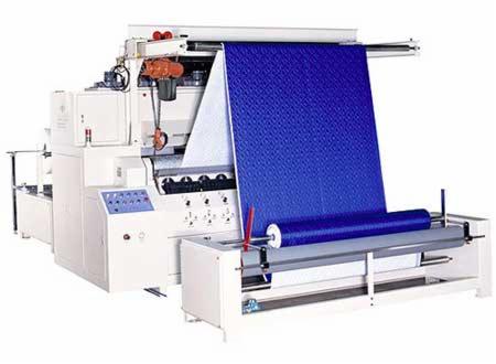 Automatyczna maszyna do pikowania tkanin z rolką niebieskiego materiału o wzorze rombów, widoczne panele sterowania i mechanizmy podawania materiału.