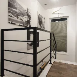 Czarna, pozioma balustrada z rurek na białym podwyższeniu z marmurowym wzorem, na tle ściany z czarno-białymi obrazami i oknem z żaluzjami.