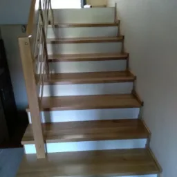 Jasne stopnie z drewna dębowego z białymi podstopnicami i metalową balustradą, widok z dołu na górę.