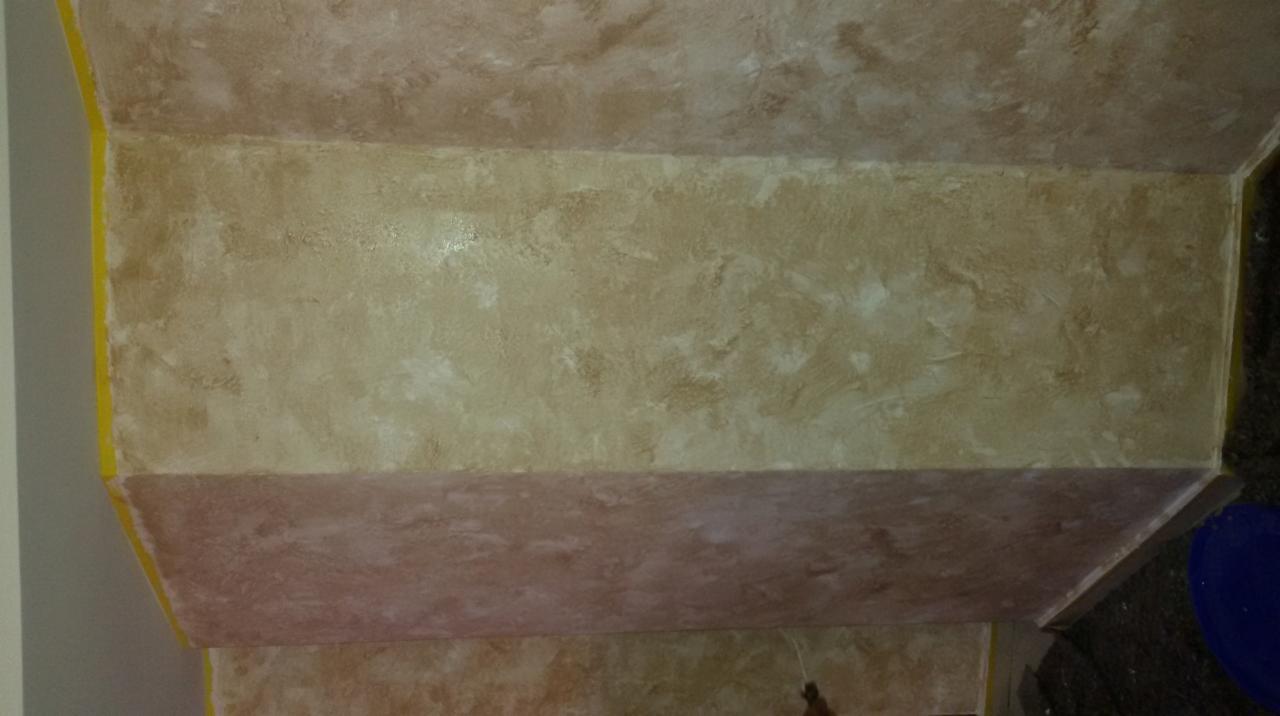 Fragment ściany i sufitu z dekoracyjną, beżowo-brązową strukturą, zabezpieczone żółtą taśmą malarską przy krawędziach.