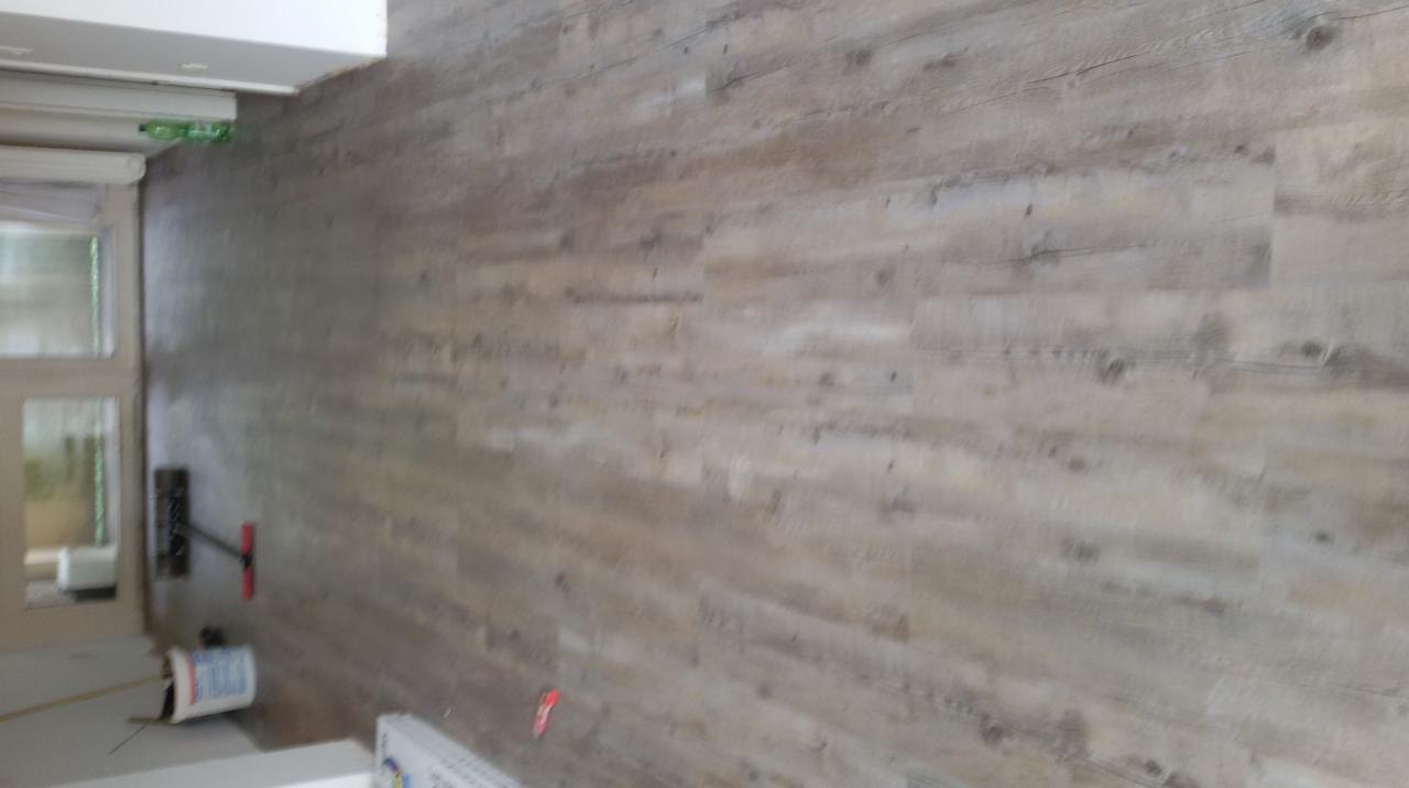 Świeżo ułożona podłoga z paneli imitujących drewno, widoczne narzędzia i puszka farby w rogu pomieszczenia, jeszcze przed ostatecznym wykończeniem.