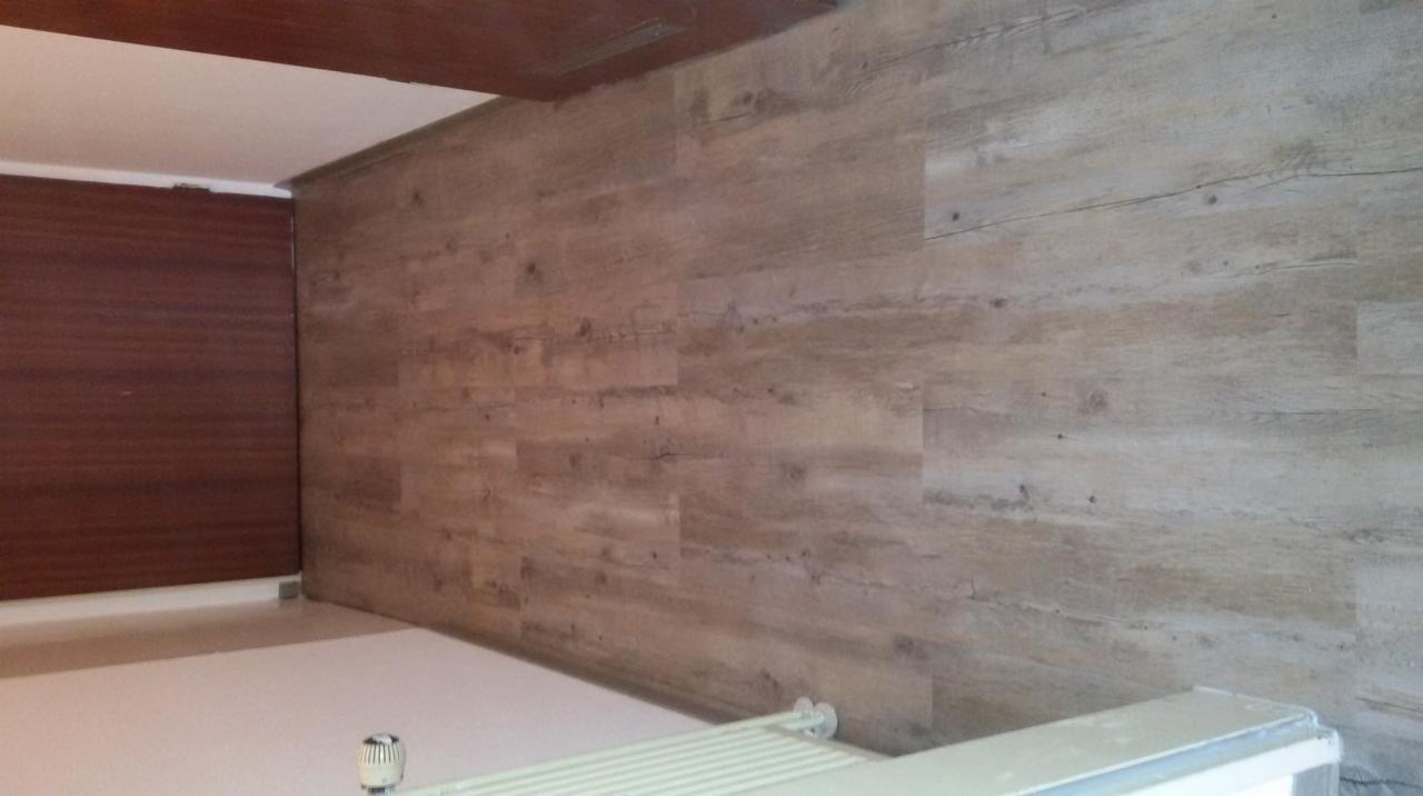 Panele ścienne imitujące drewno w jasnym odcieniu, zamontowane na ścianie w pomieszczeniu z białym sufitem i grzejnikiem.