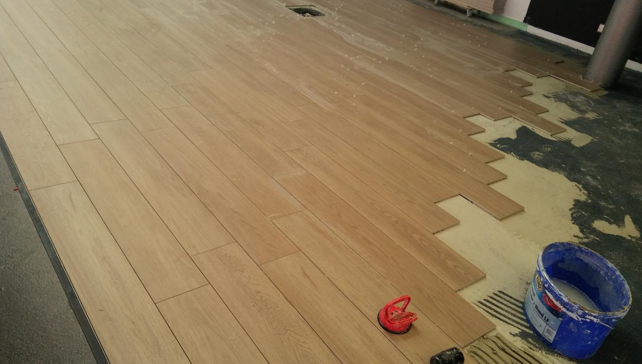 Układanie drewnianej podłogi z desek w trakcie prac, widoczny klej, przyssawka do płytek i wiadro z zaprawą.