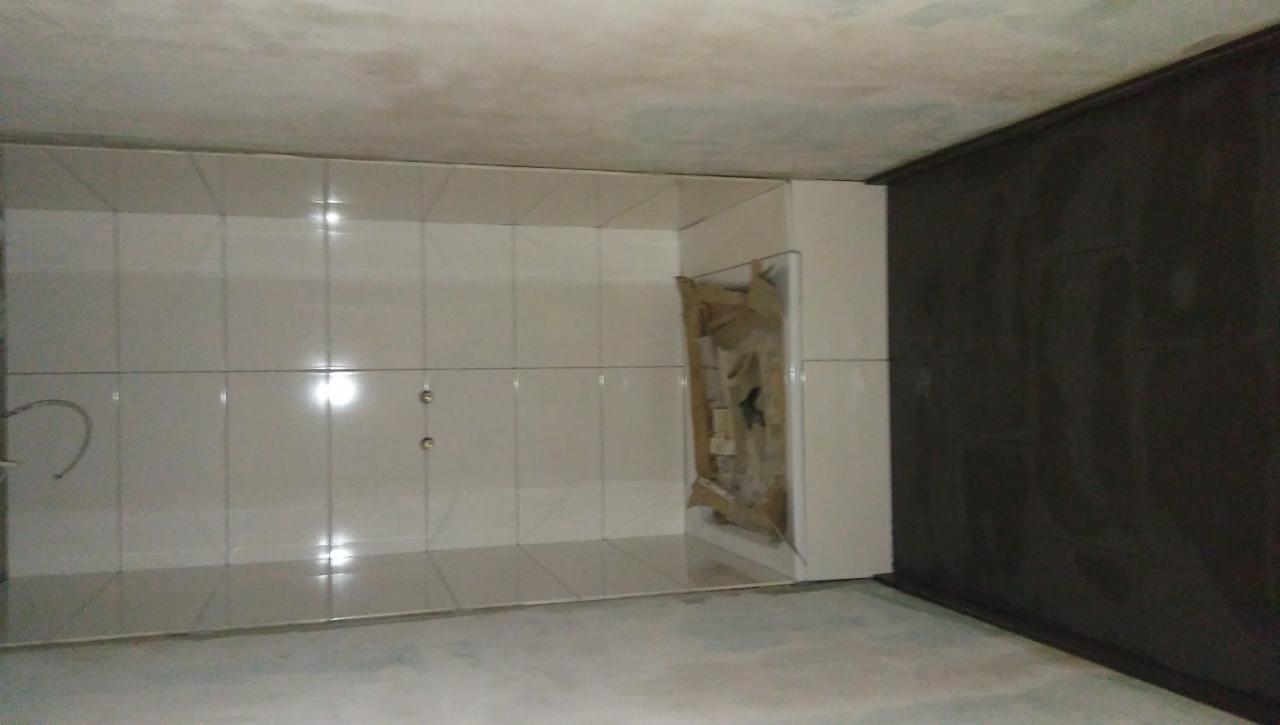 Wnętrze łazienki w trakcie wykańczania, z białymi płytkami na ścianach i podłodze, widoczne wyprowadzone instalacje wodne oraz fragment zabezpieczonego kartonem narożnika.