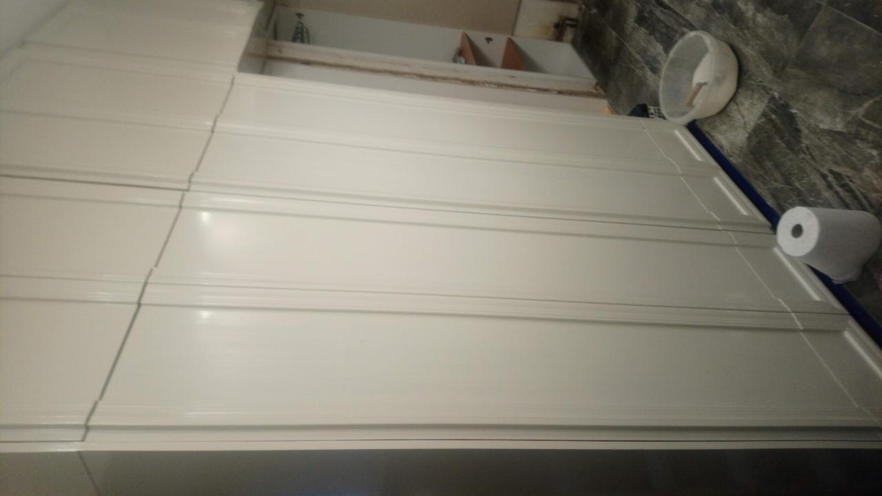 Białe, świeżo pomalowane panele ścienne z widocznym wałkiem do malowania w wiadrze i rolką papieru malarskiego na podłodze.