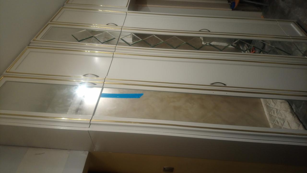 Biała szafa wnękowa z lustrzanymi wstawkami i złotymi obramowaniami, widoczna w mieszkaniu w Rogoźnie. Na jednej z szafek widoczny niebieski pasek taśmy malarskiej.