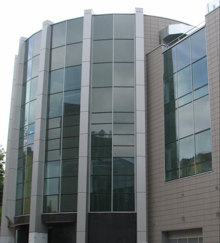 Nowoczesny budynek biurowy z przeszkloną fasadą i aluminiowymi panelami, widoczny fragment dachu z wentylacją