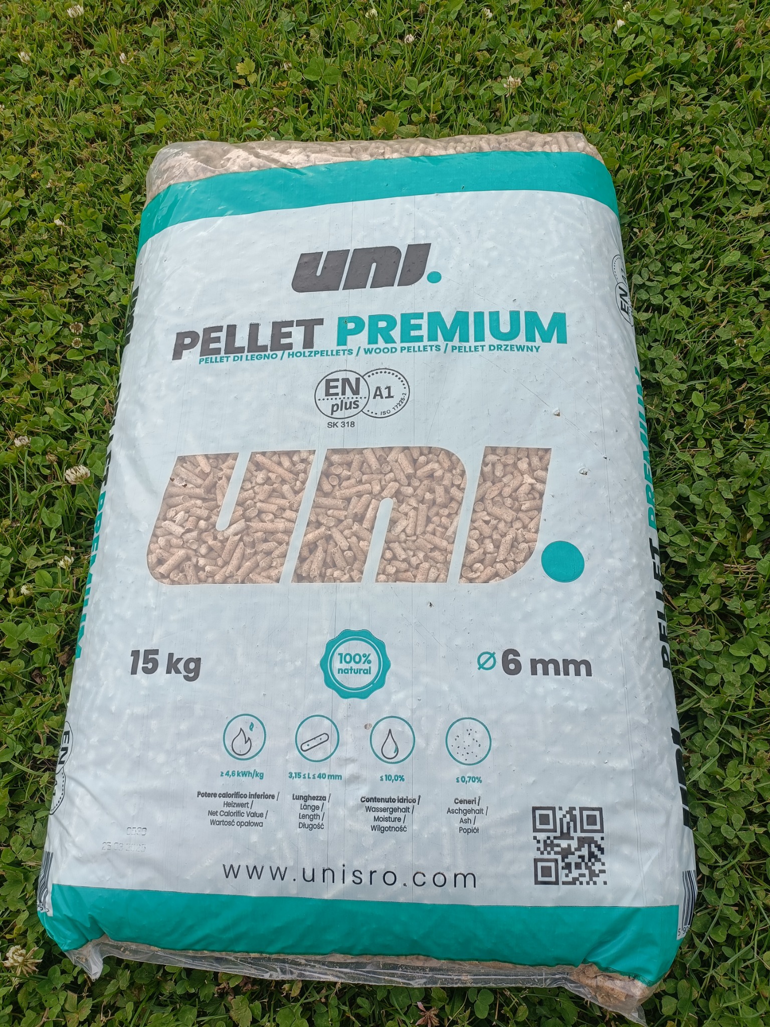 Worek pelletu drzewnego Uni. Premium 15 kg na zielonej trawie. Widoczne oznaczenia: EN Plus A1, 100% natural, średnica 6 mm. Dobrej jakości opał ekologiczny.