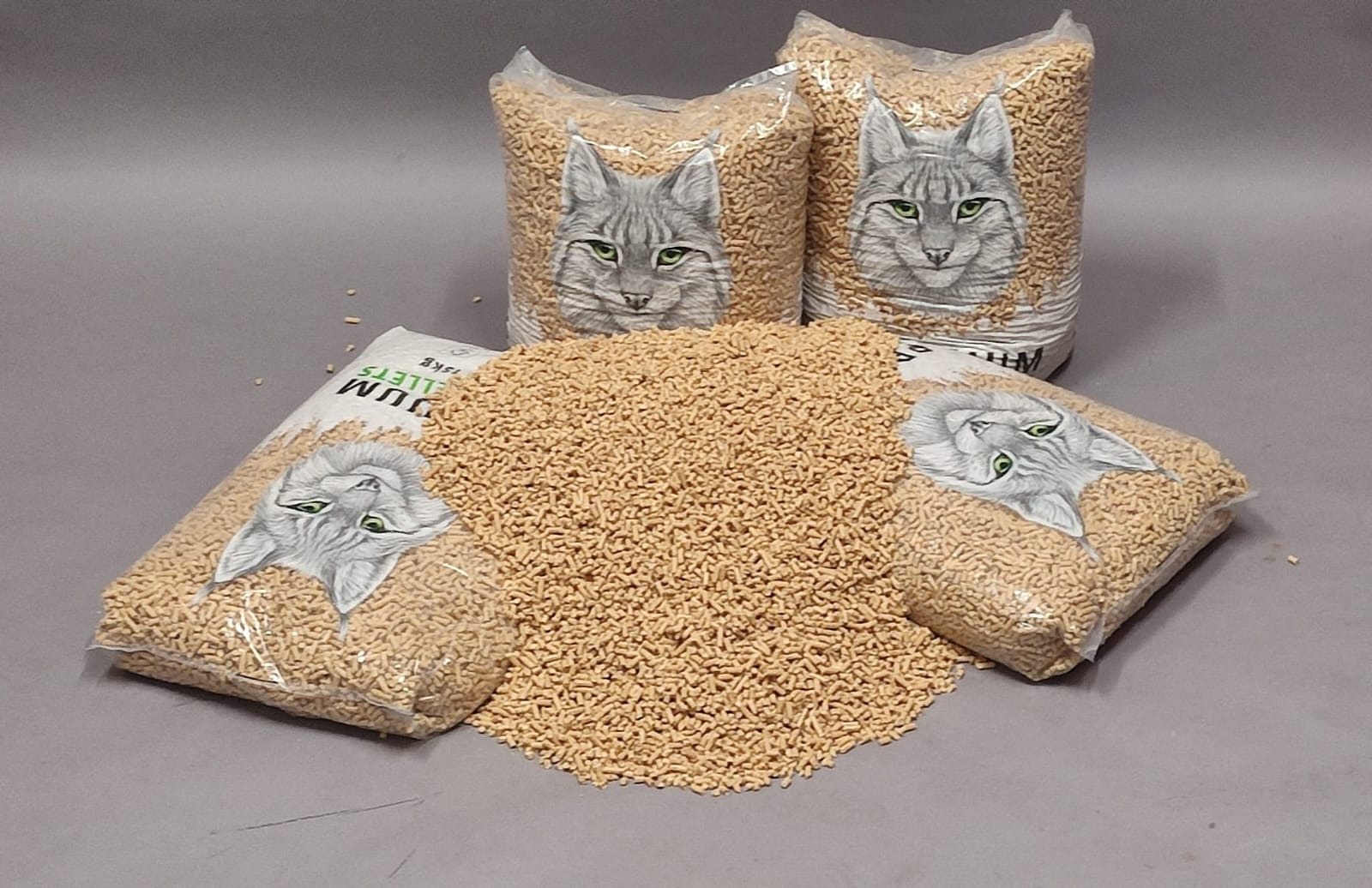Pellet z motywem kota w przezroczystych workach 15kg, ułożony na szarym tle. Widoczne granulki rozsypane obok worków. Produkt gotowy do sprzedaży.