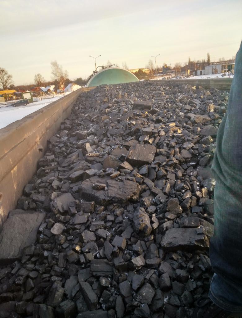 Kopalnia węgla kamiennego w zimowy dzień, widok na pryzmę surowca w betonowym korycie, w tle zielona kopuła i zabudowania.