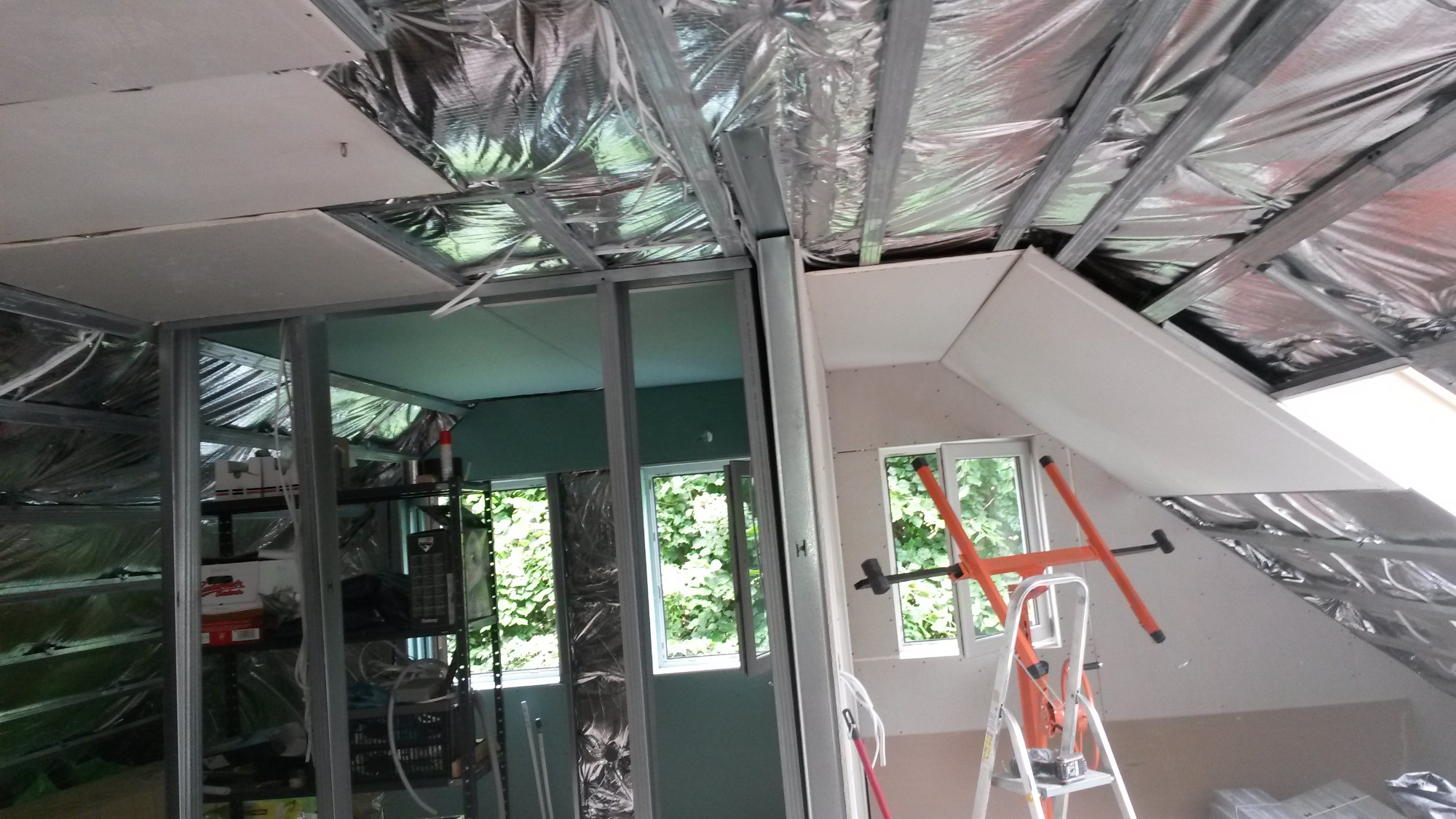 Wnętrze w trakcie wykańczania: metalowa konstrukcja ścian działowych i sufitu, częściowo obłożona płytami, widoczna izolacja folią aluminiową, drabina i rozpórka do płyt.