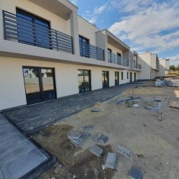 Damian Szulc Perfekt-Bud - Nowoczesne domy w zabudowie szeregowej z ciemną kostką brukową na etapie układania, widoczne nieułożone kostki i piasek.