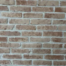 Dekoracyjna ściana z cegły w odcieniach czerwieni i beżu z jasną fugą, imitująca starą cegłę.