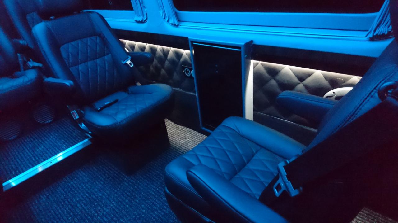 Wnętrze luksusowego busa z pikowanymi skórzanymi fotelami, podświetleniem LED i eleganckim wykończeniem ścian.