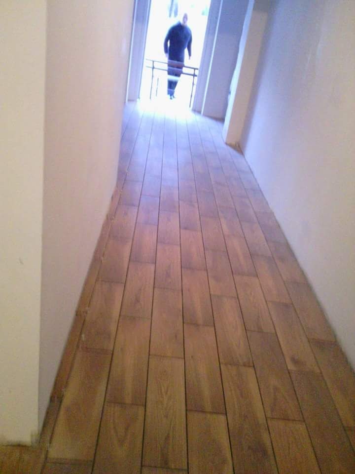 Ułożona podłoga z paneli imitujących drewno w korytarzu, widoczna osoba wychodząca na balkon w tle.