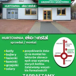 Budynek hurtowni instalacyjnej z zielonymi szyldami informującymi o sprzedaży i montażu kotłów, bojlerów, łazienek, kominków, grzejników, solarów oraz pozyskiwaniu dotacji na kolektory słoneczne.