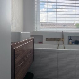 Egad - Nowoczesna łazienka z drewnianą szafką pod umywalką, wanną obudowaną płytkami z poziomymi żłobieniami i złotą armaturą wbudowaną w ścianę, widok przez okno z żaluzjami na dach budynku.