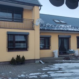 ALUPLASTI S.C. MAGDALENA I PIOTR GAZDA - Dom z oknami zabezpieczonymi roletami antywłamaniowymi w kolorze antracytowym. Zima, śnieg na dachu i chodniku. Balustrada balkonowa z metaloplastyki.