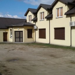 ALUPLASTI S.C. MAGDALENA I PIOTR GAZDA - Żółty budynek z brązowymi roletami zewnętrznymi, widoczne klimatyzatory na ścianie. Ujęcie z zewnątrz, w tle błękitne niebo.