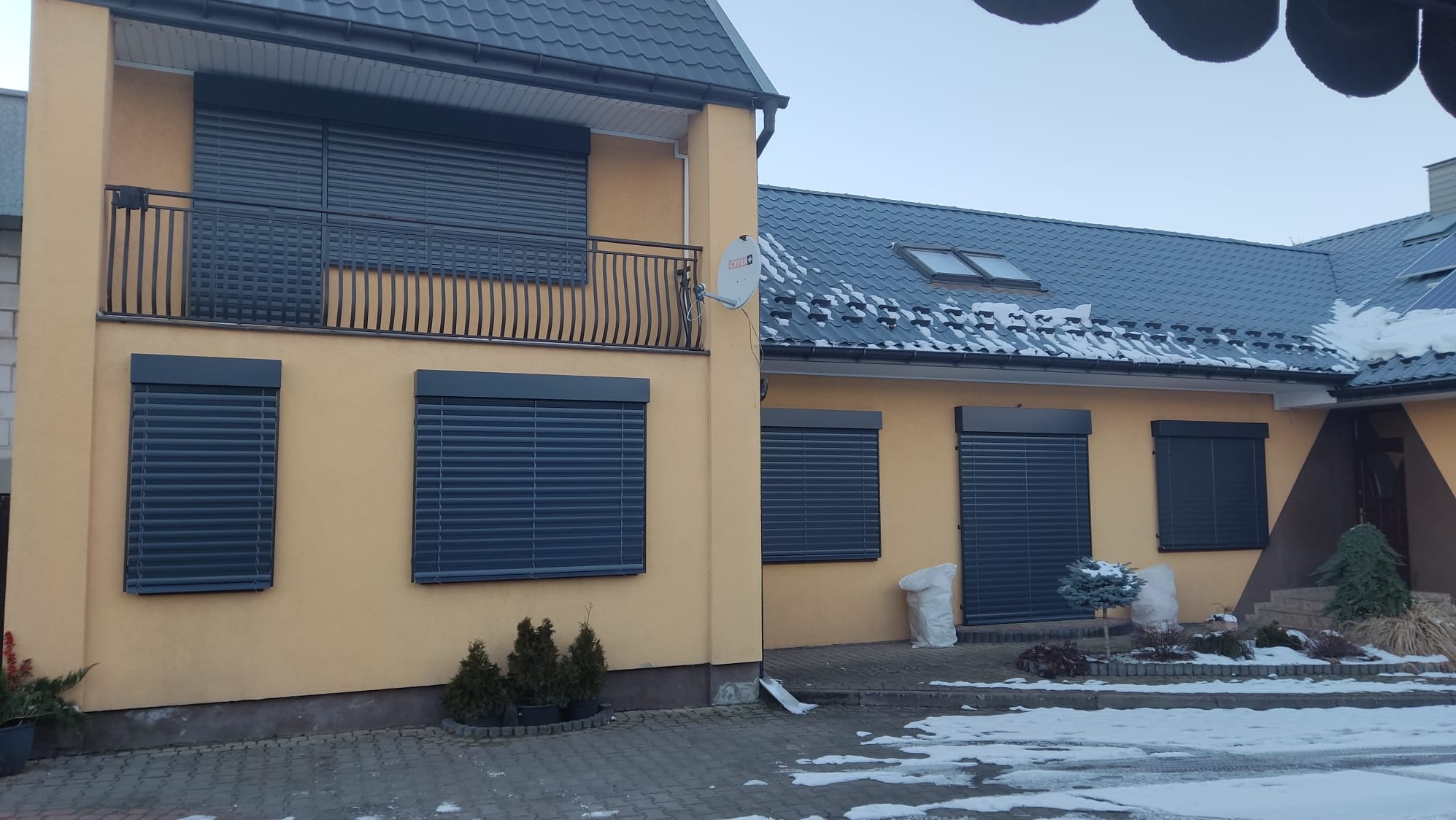 Żaluzje fasadowe w kolorze antracyt na oknach domu w Stężycy. Widoczne detale architektoniczne i zimowy krajobraz. Zamknięte rolety zapewniają prywatność i bezpieczeństwo.