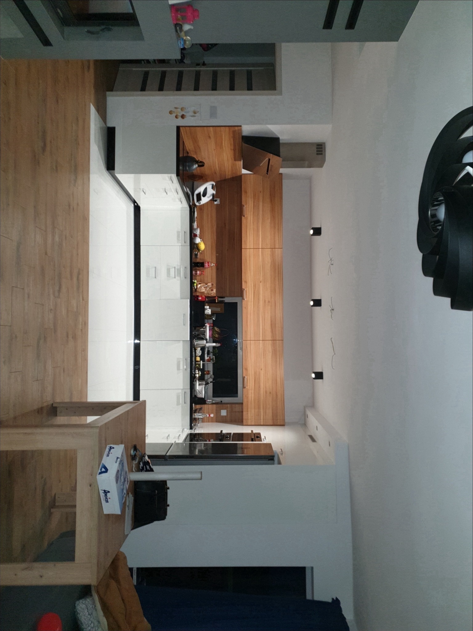 Nowoczesna kuchnia z drewnianymi i białymi szafkami, czarnym blatem i drewnianą podłogą, widok z góry z perspektywy antresoli.