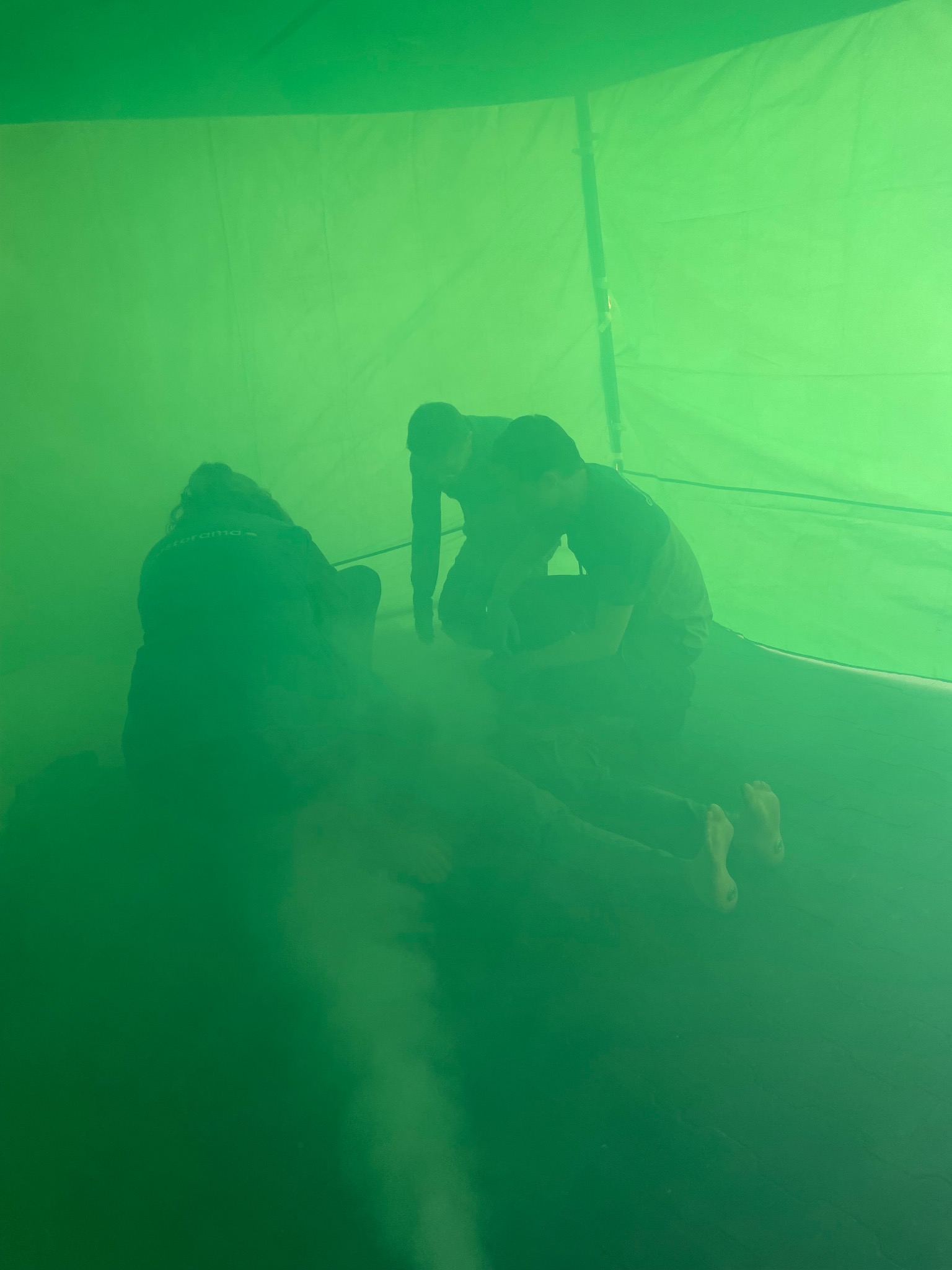 Scena wewnątrz zielonego namiotu: instruktorzy demonstrujący resuscytację na manekinie, widoczne bose stopy osoby pozorującej poszkodowanego.