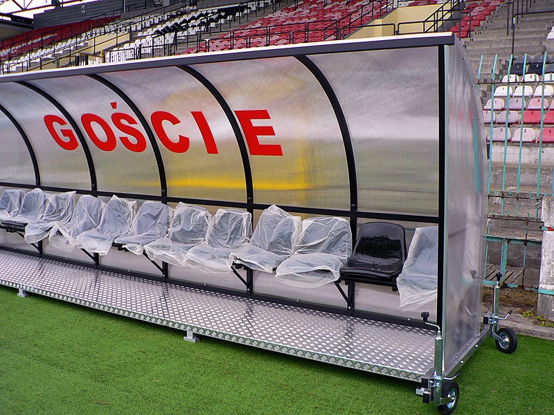 Przenośna wiata stadionowa dla gości z przezroczystym zadaszeniem, siedzeniami w folii ochronnej i aluminiową podłogą na kółkach.