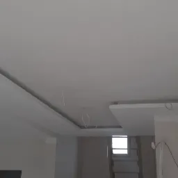 Nowoczesny sufit podwieszany z zamontowanym oświetleniem punktowym i wystającymi kablami instalacji elektrycznej w trakcie remontu.