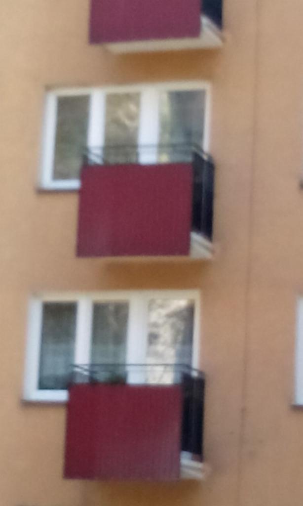 Balkony z czerwoną osłoną, widok z dołu, budynek mieszkalny z białymi oknami.